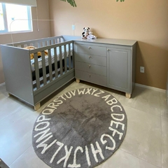 tapete infantil redondo alfabeto cinza com letras brancas em um quarto de bebê com berço ao fundo
