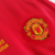 Detalhe do bordado do escudo do Manchester United na camisa vermelha de manga longa de 2007.