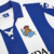 Camiseta de futebol da Real Sociedad com listras azuis e brancas, destacando o emblema do clube.