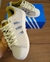 Tênis Adidas Superstar em tons claros, com detalhes prateados e caixa azul ao fundo.