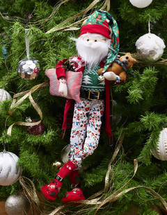 Muñeco de Santa Claus con pijama y bata de cuadros, sosteniendo un osito de peluche y una almohada.