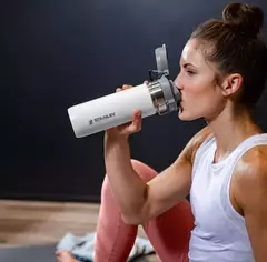 Mujer bebiendo de una botella térmica de acero inoxidable blanca de 709 ml, diseñada para ser compacta y a prueba de fugas.