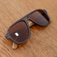anteojos de sol de madera (patillas) y acetato color marrón rayado oscuro y claro (frente) estilo aviador modelo patagonia marca nomade sobre fondo de madera