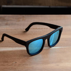 anteojos de sol de acetato color negro mate con lentes espejados polarizados color azul modelo Tulum PA marca Nómade sobre fondo de madera