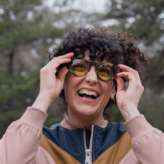 mujer sonriente con anteojos de madera (patillas) y acetato (frente) simil carey con lentes color amarillo, forma redonda, estilo oversized modelo Skorpios TINT marca Nomade