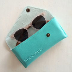 estuche para anteojos de cuero sintetico color turquesa con cierre de boton marca Nomade abierto con anteojos de sol en su interior fondo blanco