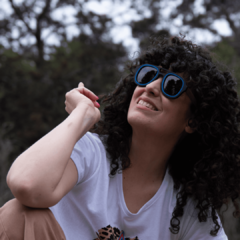 mujer sonriendo con anteojos de sol de madera (patillas) y frente de acetato negro con aro incrustado color azul, con lentes grises modelo Hanoli BOLD estilo aviador marca Nómade