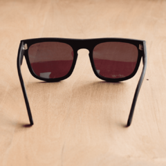 anteojos de sol de acetato color negro mate con lentes espejados polarizados color azul modelo Tulum PA marca Nómade sobre fondo de madera vista posterior