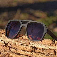 anteojos de madera (patillas) y acetato (frente) color negro tipo aviador con lentes de sol polarizados modelo Barker marca Nómade (vista anteojo apoyado sobre un trozo de madera) 