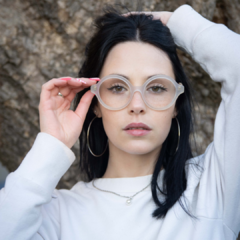 Mujer con anteojos de madera (patillas) y acetato (frente) color cristal de forma redondeada para colocar lentes de aumento modelo Viena marca Nómade