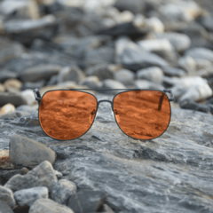 anteojos de sol de metal color negro mate con lentes color ambar estilo aviador modelo Aconcagua marca Nomade con fondo de piedras