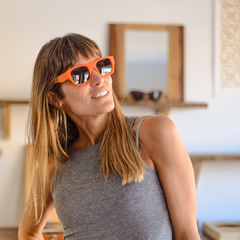 mujer joven con pelo largo rubio con flequillo con anteojos de sol de estilo rectangular color naranja fluo modelo Corcega marca Nomade