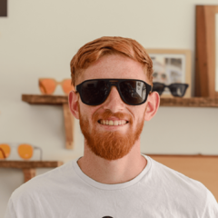 hombre joven de piel blanca y pelo rojo con anteojos de sol estilo aviador color negro mate con lentes color gris modelo Patagonia PA Lite marca Nomade vista frente