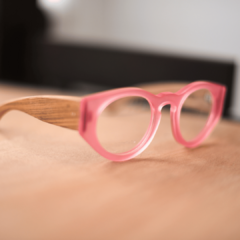 anteojos de acetato rosa brillante traslucido (frente) y patillas anchas de madera con forma redondeada modelo Skorpios marca Nomade sobre fondo de madera vista derecha