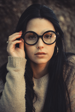 Mujer luciendo anteojos de madera (patillas) y acetato (frente) color negro de forma redondeada para colocar lentes de aumento modelo Viena marca Nómade