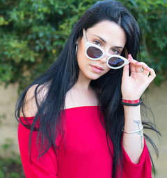 Mujer luciendo anteojos de madera (patillas) y acetato (frente) color blanco de forma redondeada con lentes de sol polarizados modelo Chalten marca Nómade (vista con anteojo a medio poner en la cara)