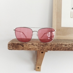 anteojos de sol de metal color cromo estilo aviador rectangular con lentes color rosa modelo La Juanita marca Nomade sobre repisa de madera y fondo blanco
