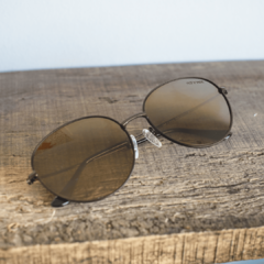 anteojos de sol de metal de forma redonda color cobre con lentes polarizados espejados color marron modelo los pioneros marcca nomade con fondo de madera