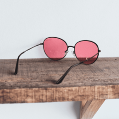 anteojos de sol de metal de forma redonda color cobre con lentes color rosa modelo los pioneros marca nomade con fondo de madera