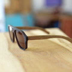 anteojos de sol de madera (patillas) y acetato color marrón rayado oscuro y claro (frente) estilo aviador modelo patagonia marca nomade sobre fondo de madera vista de perfil