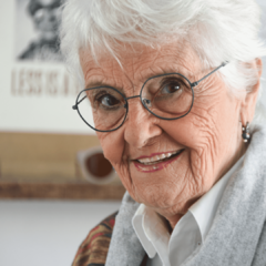 mujer mayor de pelo blanco y corto sonriendo con anteojos de metal en color verde mate de forma redondeada modelo Lanin marca Nómade vista medio perfil