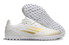 Chuteira Society Adidas F50 Club em branco com detalhes dourados e sola com cravos.