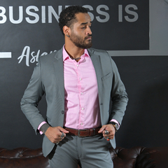 Hombre con traje gris y camisa rosa, posando con confianza en un entorno profesional.