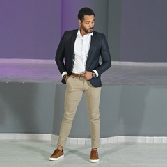 Hombre posando con un blazer petróleo slim fit, camisa blanca y pantalones beige, calzado deportivo en un ambiente moderno.