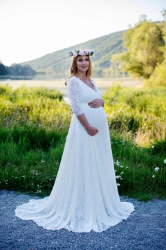 Noiva gestante usando um vestido de renda branco com decote em V, posando em um ambiente natural, ideal para casamentos no campo ou na praia.