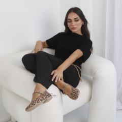 Mujer sentada en un sofá blanco, luciendo chatitas de estampado leopardo y un atuendo negro.