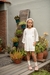 Nena con vestido Calao off white, de gasa de algodón con puntilla y pompones en cintura y mangas amplias.