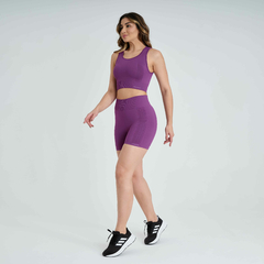 Mulher usando um top feminino roxo da Marcio May, combinado com shorts, caminhando com tênis esportivos.