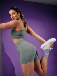 Modelo usando shorts femininos verdes mesclados da linha Marcio May Sports, posando com uma perna esticada e um sorriso, em um fundo roxo.