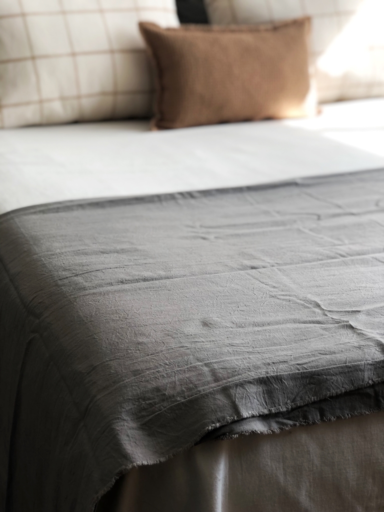 Banco de madera en el pie de la cama con ropa de cama gris y manta