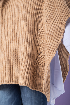 Poncho en lana tejida con detalle de cuello polera. Abierto a los costados. En color tostado.