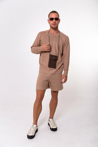 Modelo masculino usando uma raglan básica bege, com um shorts bege, um crossbody marrom da marca e um óculos escuro